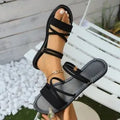 Women's black sandals with a flip-toe buckle and flat cross strap on a rubber sole.