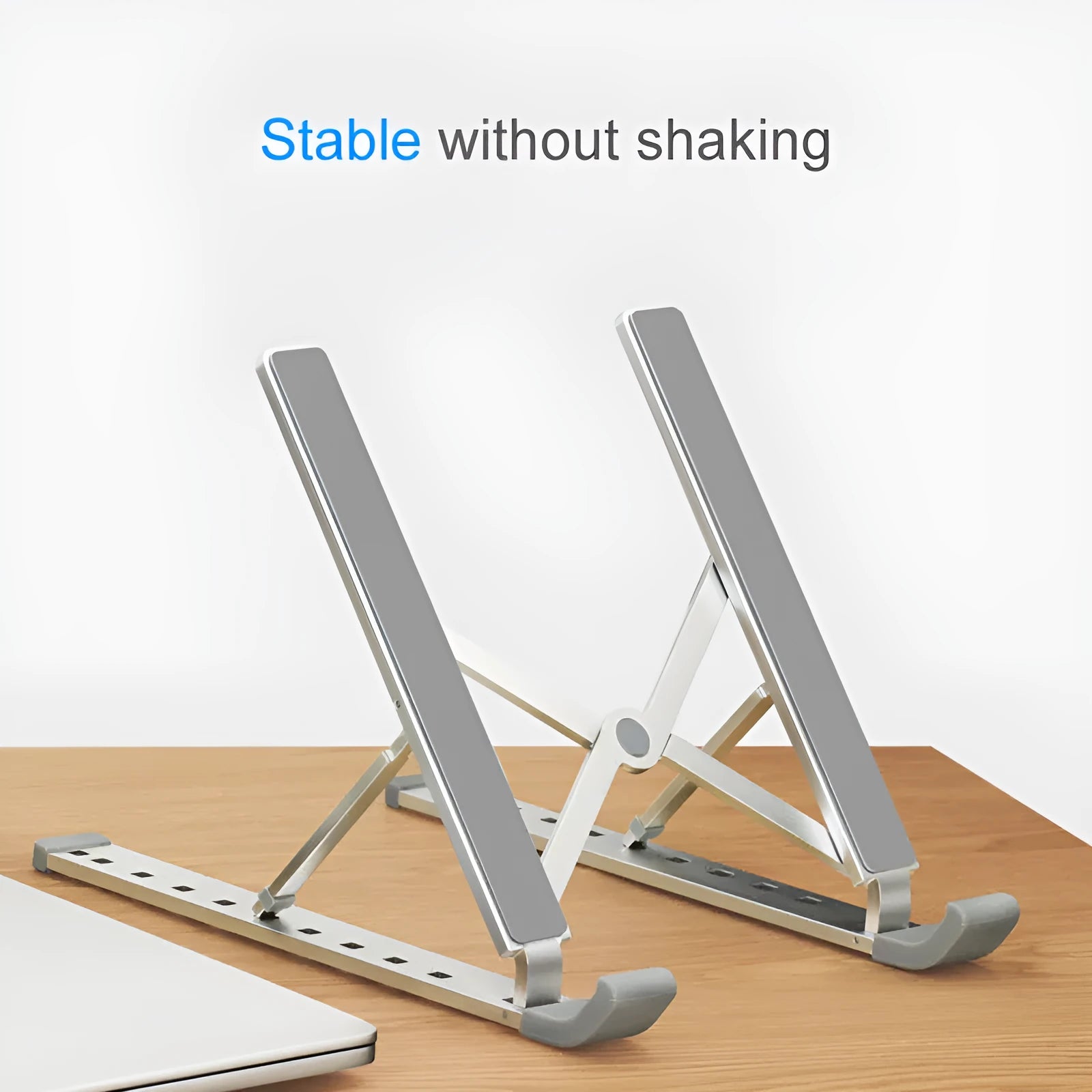 Folding aluminium laptop stand in silver, open and holding a laptop, with non-slip silicone pads visible