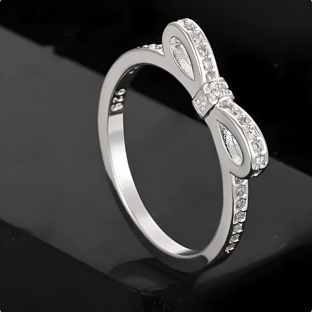 Silver coloured bow-shaped ring with sparkling rhinestone crystals on a model's hand.