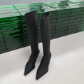 Women's black pointed toe below-the-knee boots with a stiletto heel and back zip on a neutral background.