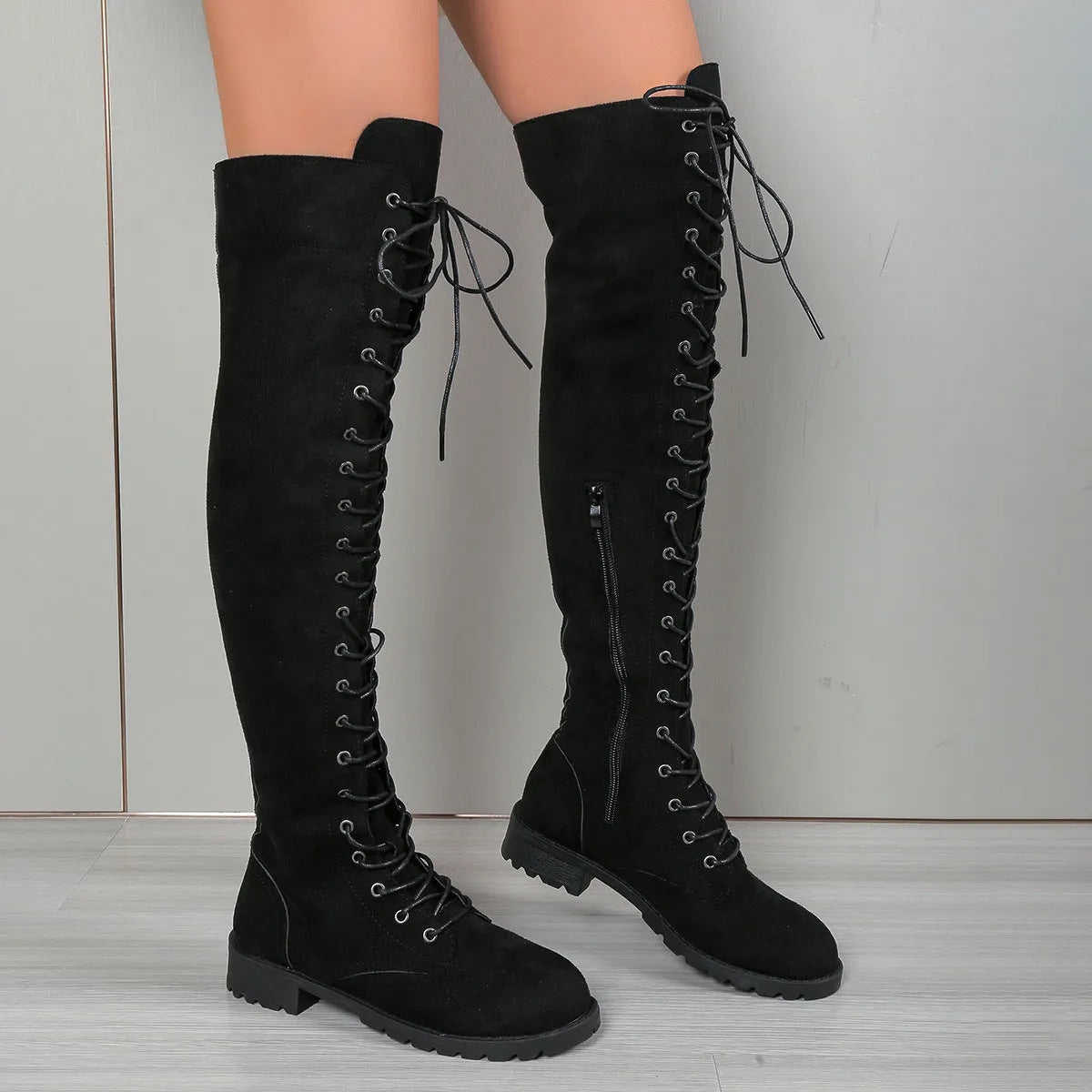Black lace-up over-the-knee boots with a round toe, flat rubber sole, and decorative leather stitching on the upper.