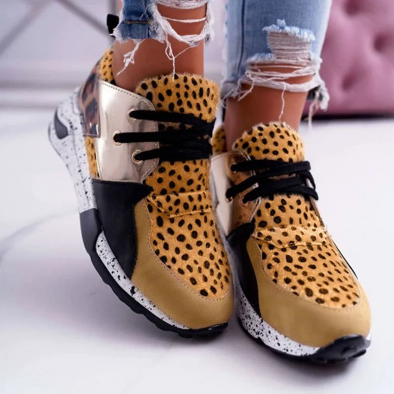Women's black suede wedge sneakers with a round toe and low-cut design on a wooden floor.