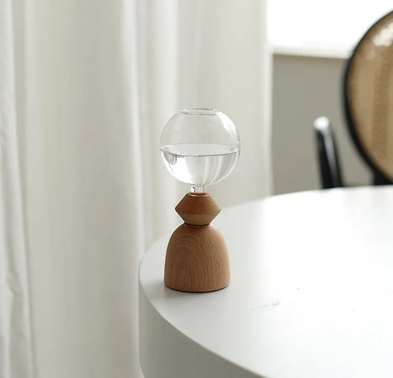 Small clear geometric bubble glass vase on a wooden base, shown with a single flower stem.