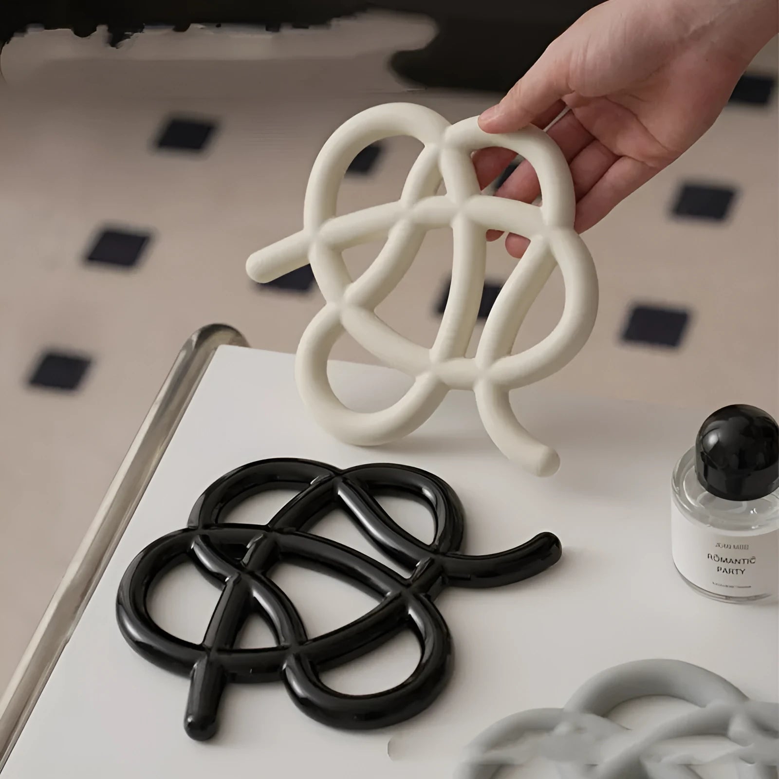 Irregular-shaped ceramic heat proof mat in grey with a curved hook for hanging, sitting on a wooden table.