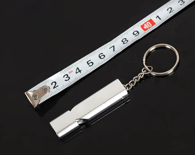 Close-up of a silver aluminium alloy double-hole outdoor survival whistle on a dark background.