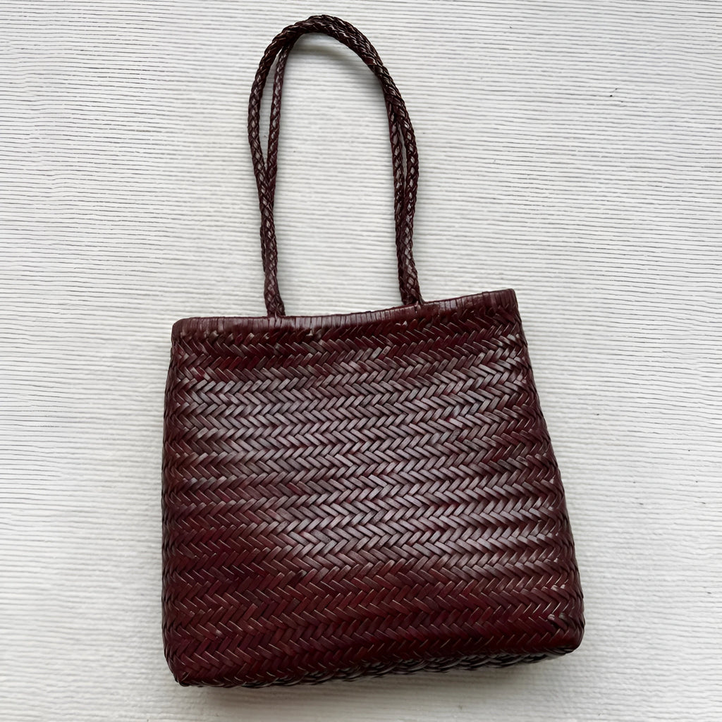 Brown handmade woven leather tote bag with a three-dimensional front pocket and shoulder strap.