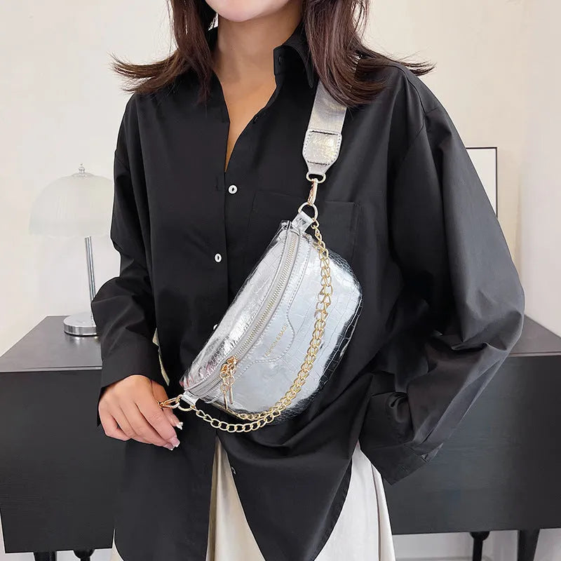 Shiny hard-shell PU chest bag with wide shoulder strap, chain detail, and internal pockets in silver colour
