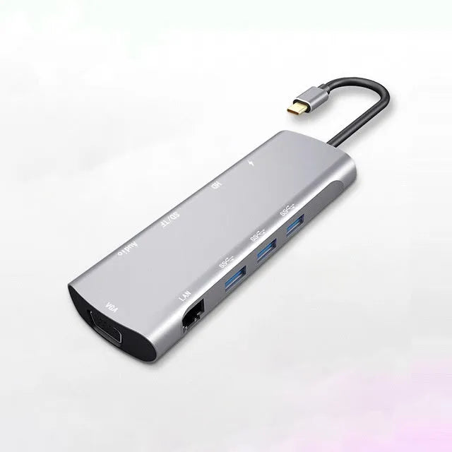 Grey aluminium USB-C docking station with HDMI, VGA, USB 3.0, and PD charging ports on a desk.