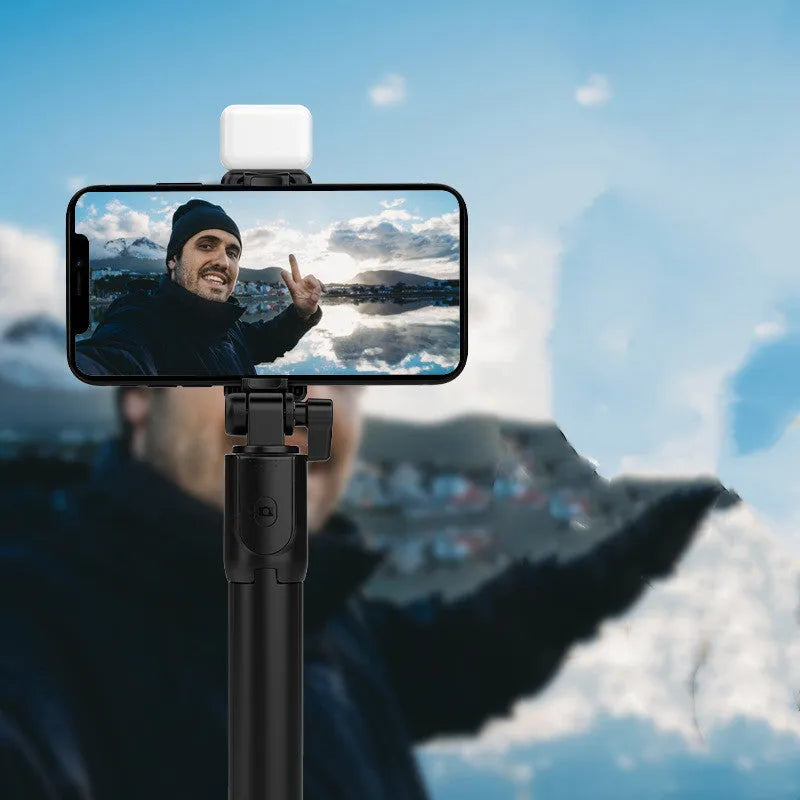 Black Bluetooth selfie stick with extended tripod legs holding an iPhone, showcasing its 360-degree rotating phone holder.
