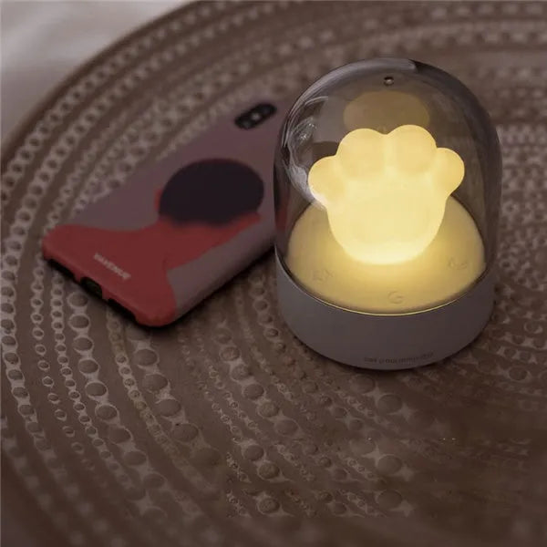 Pink cat paw shaped USB rechargeable night light with soft glow on a desk.