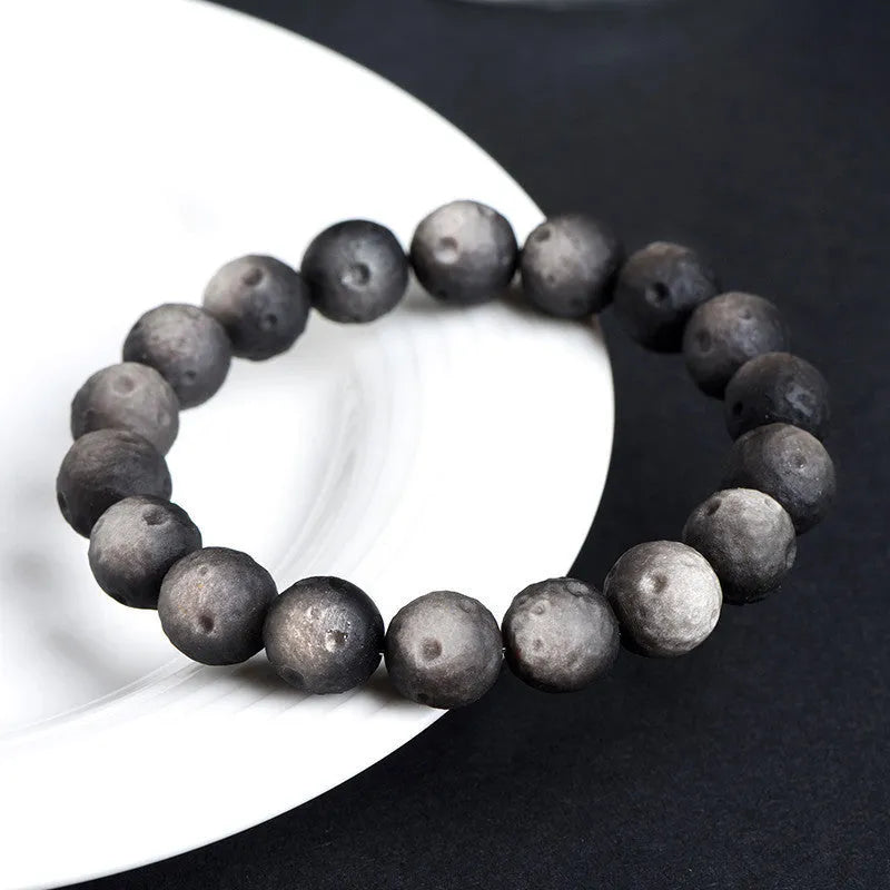 Close-up of an obsidian crater ball bead bracelet in a gold meteorite finish, showing its textured spherical beads.