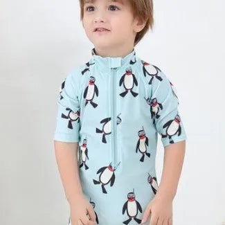 Boy's penguin print long sleeve swimsuit top and matching swim cap set on blue background