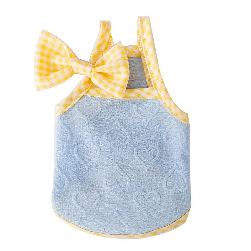 Small dog wearing a blue vest with heart texture and bow suspenders, showing adjustable elastic sides.
