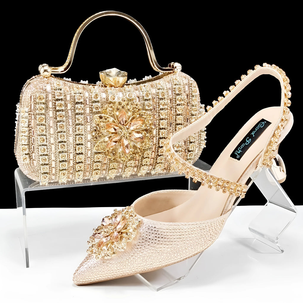 Women's black high heel shoes with rhinestone flowers and an ankle chain, next to a matching hard clutch bag.