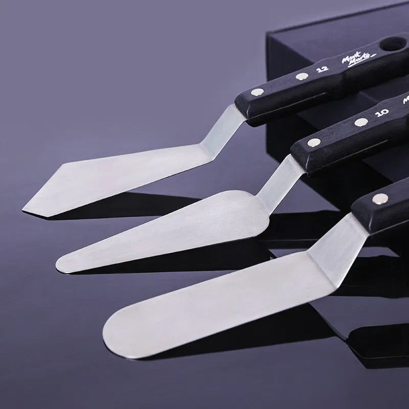 Three stainless steel painting palette knives with different blade shapes on artist's palette