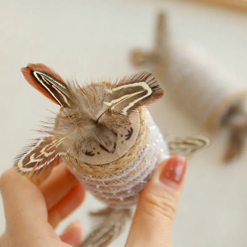 Beige interactive cat toy with hemp rope scratching post, colourful feathers, and a rolling sound mechanism.