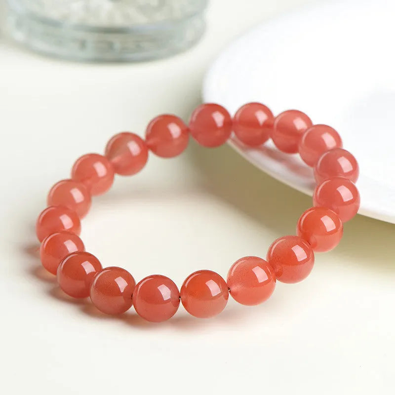 Natural cherry red agate bracelet with hand-polished beads on a wrist, showing colour variation and secure clasp.
