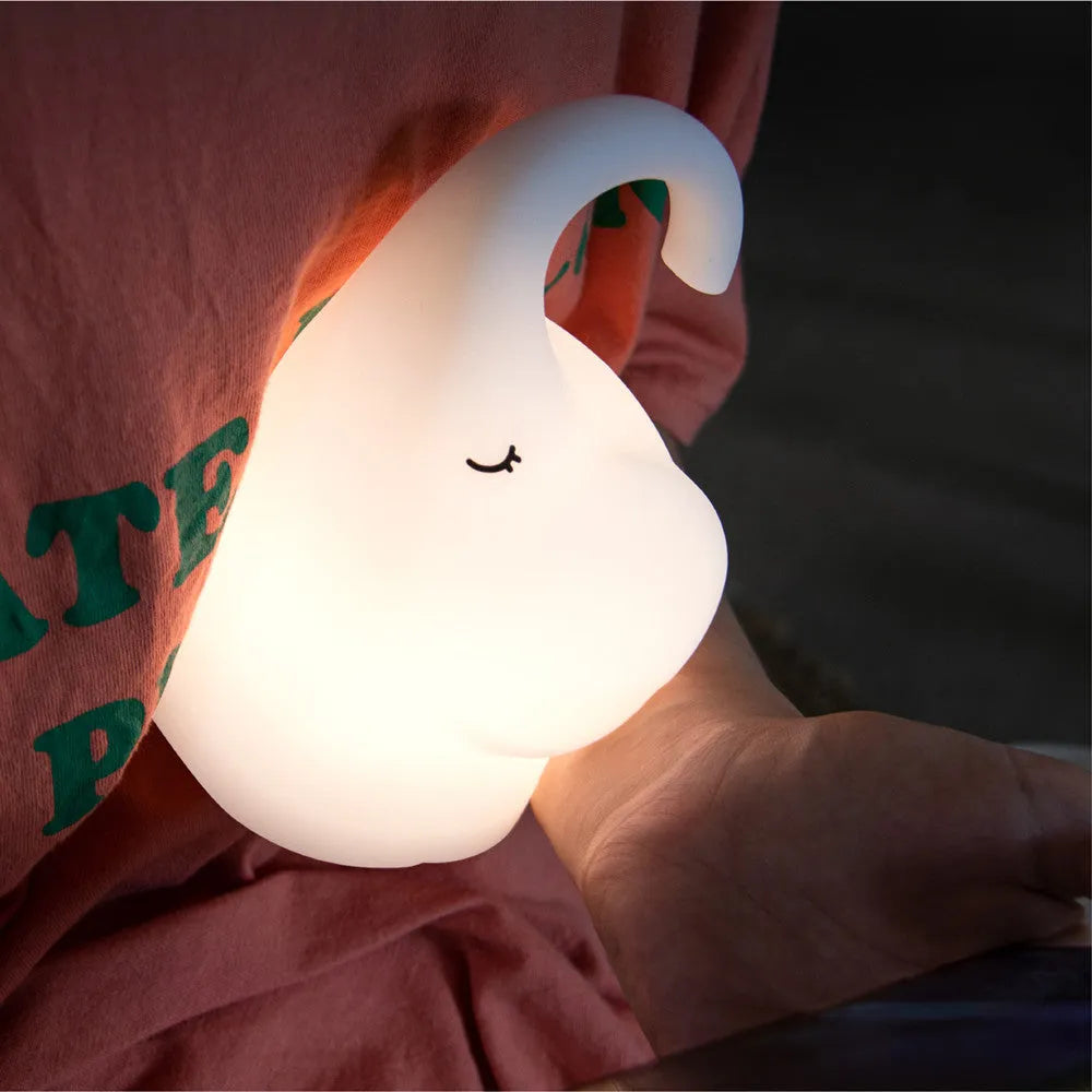DOMI Elephant shaped silicone night light with warm white glow on a bedside table.
