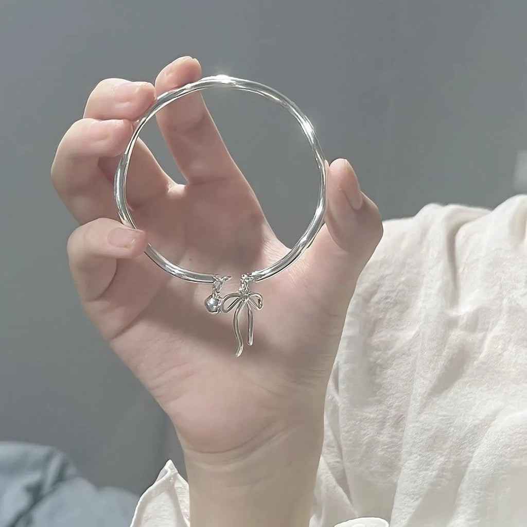 Silver adjustable bracelet with a detailed bow charm on a model's wrist, showing the adjustable clasp.