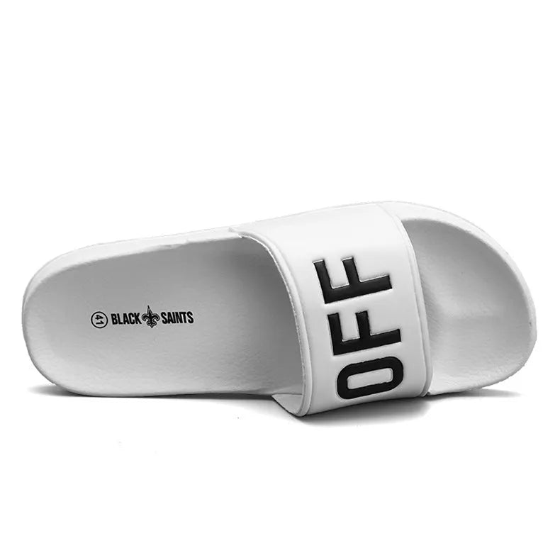 Men's black open-toe slippers with a textured rubber sole and soft viscose upper, shown on a wooden floor.