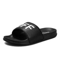 Men's black open-toe slippers with a textured rubber sole and soft viscose upper, shown on a wooden floor.