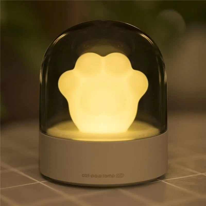 Pink cat paw shaped USB rechargeable night light with soft glow on a desk.