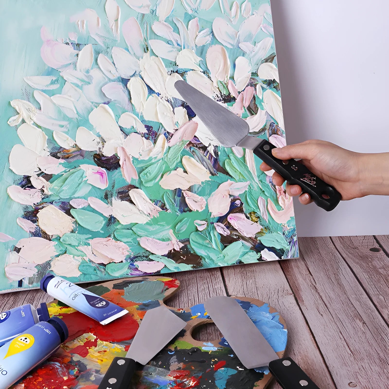 Three stainless steel painting palette knives with different blade shapes on artist's palette