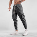 Men's loose-fit light grey cotton trousers with tapered legs and tied ankle cuffs, showing multi-pocket detail.