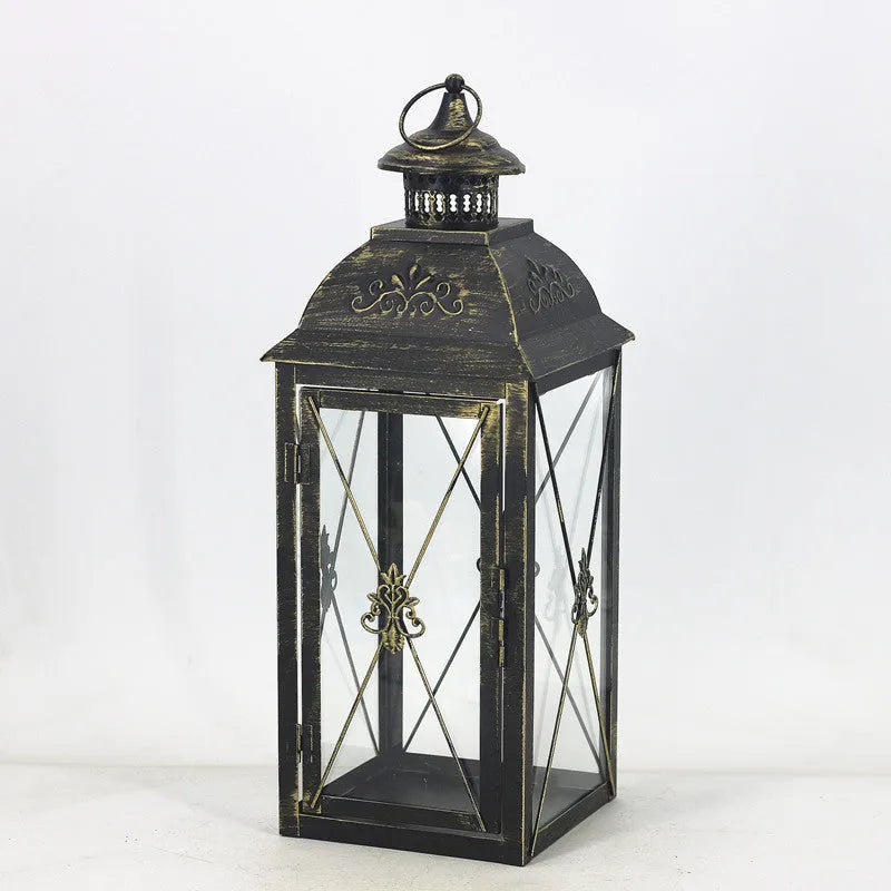 Black wrought iron floor-standing storm lantern with clear tempered glass panels on a garden patio.