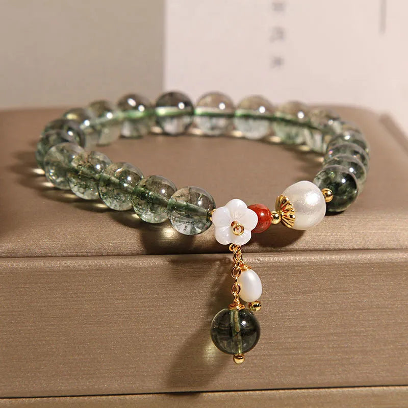 Women's green phantom quartz crystal bracelet with small shell flower accent on wrist.