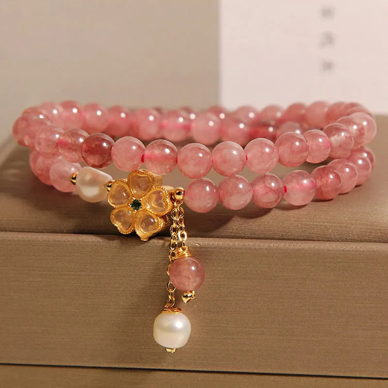 Women's double ring bracelet with strawberry quartz four-leaf clover charms on wrist.