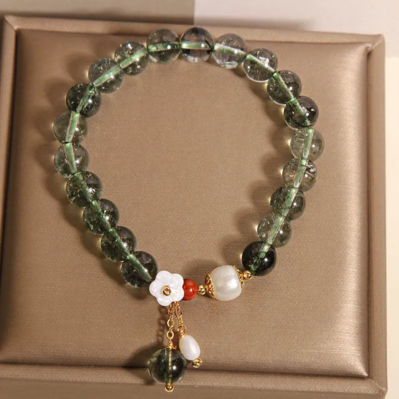 Women's green phantom quartz crystal bracelet with small shell flower accent on wrist.