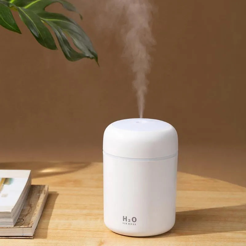 Pink USB desktop humidifier with colourful lights and water tank on wooden surface