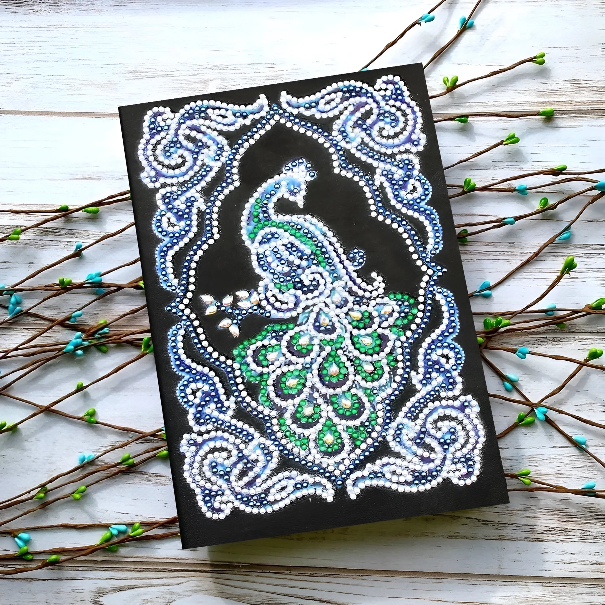 Black A5 diamond painting notebook open, showing journal pages alongside shaped and bright sparkling drills.
