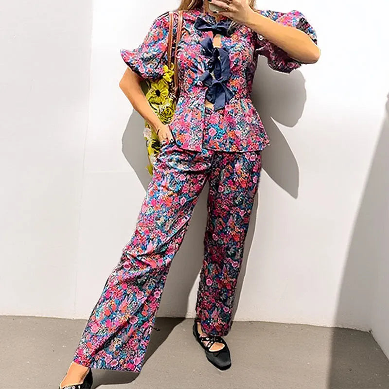 Women's floral print polyester trousers suit with tie-neck blouse and puff sleeves.
