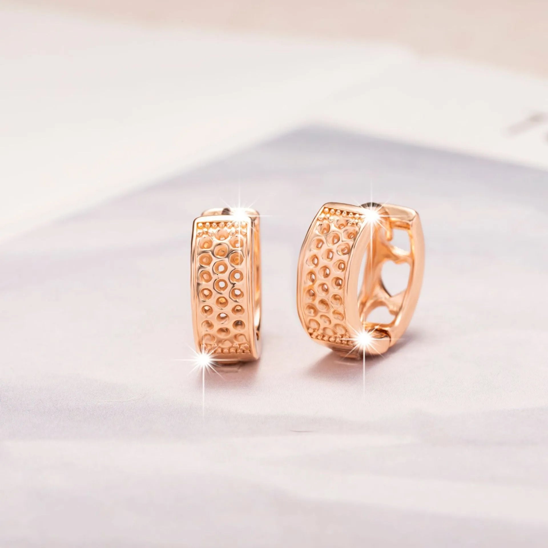 Close-up of a pair of rose gold circular hoop earrings with three small hollow heart shapes cut out of each band.
