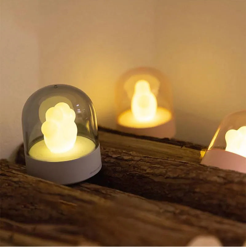 Pink cat paw shaped USB rechargeable night light with soft glow on a desk.