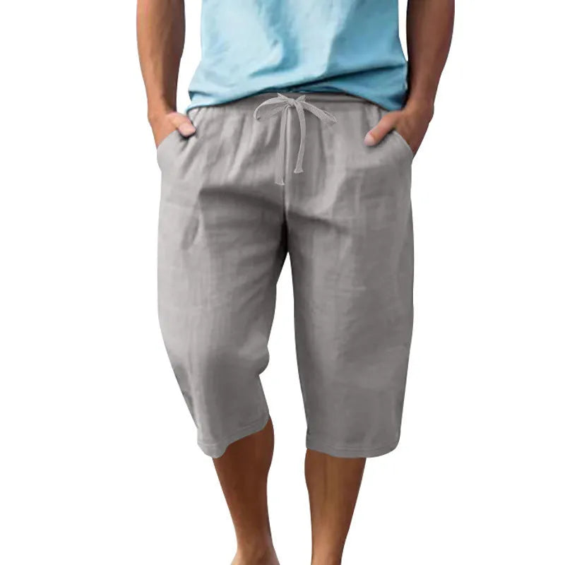 Man wearing loose-fit, solid-colour linen shorts in a light blue shade, showing the cropped length and drawstring waist.