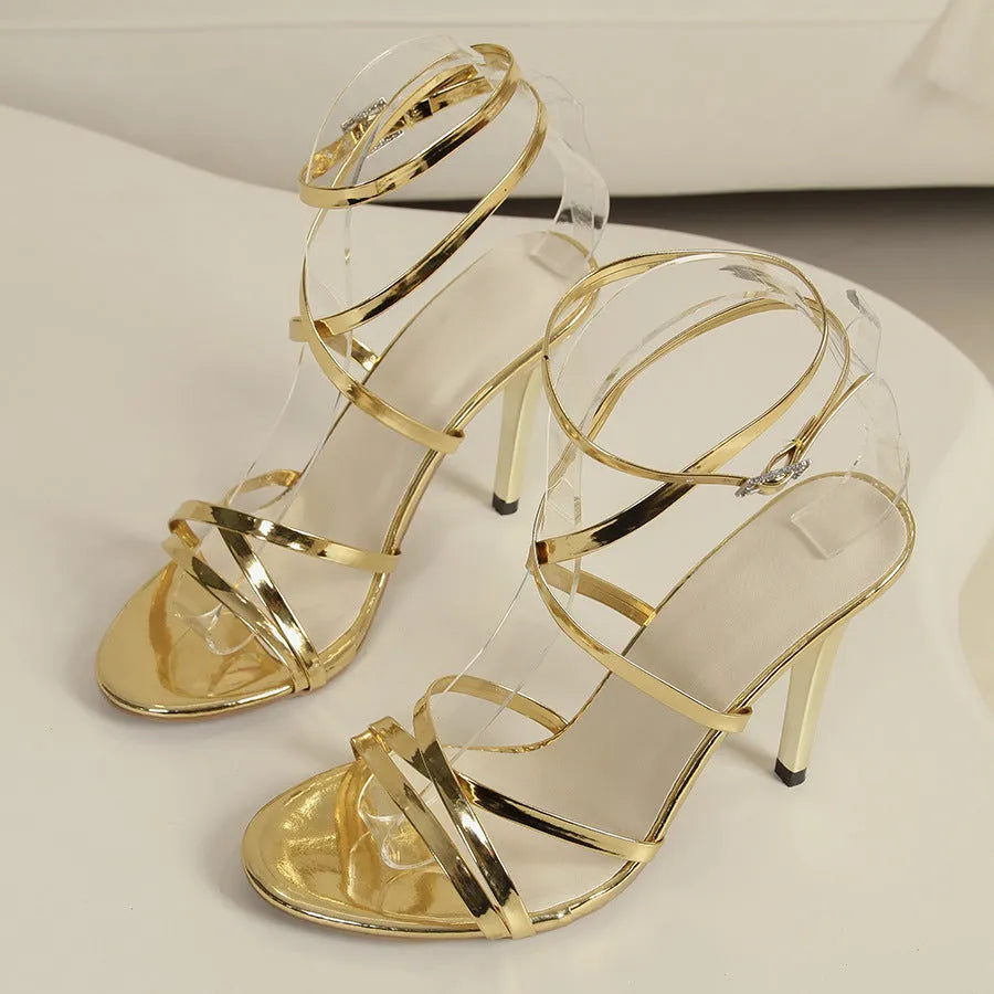 Gold women's stiletto sandals with a cross-strap buckle fastening and a black rubber sole.