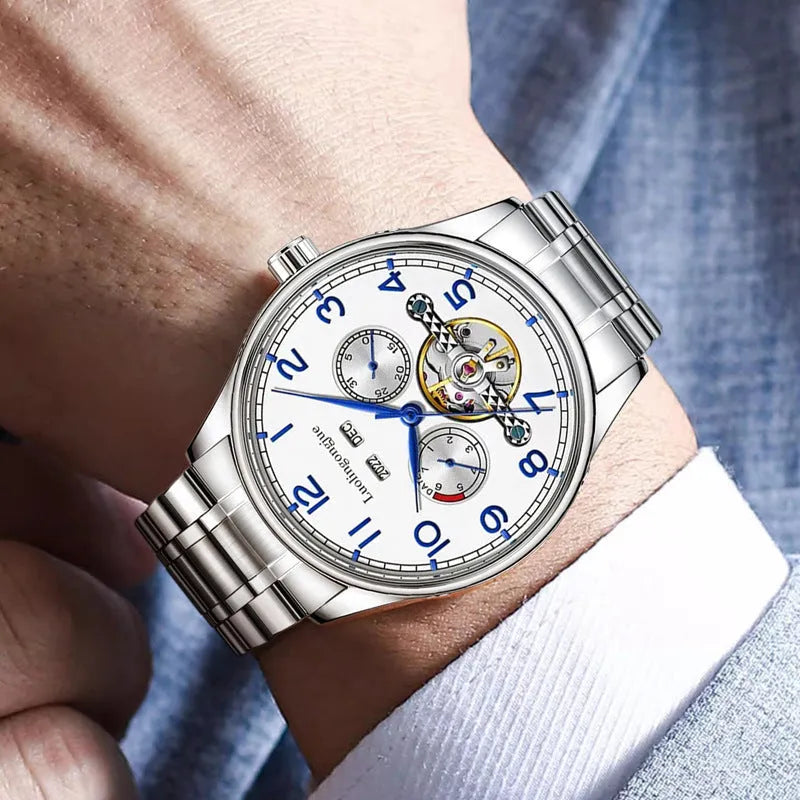 Men's stainless steel mechanical watch with leather strap and butterfly buckle on a business suit cuff.