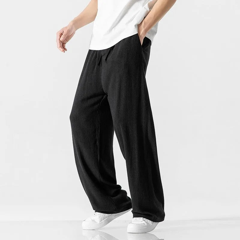 Man wearing beige straight-leg cropped bamboo fibre trousers with a drawstring waist on a summer day.