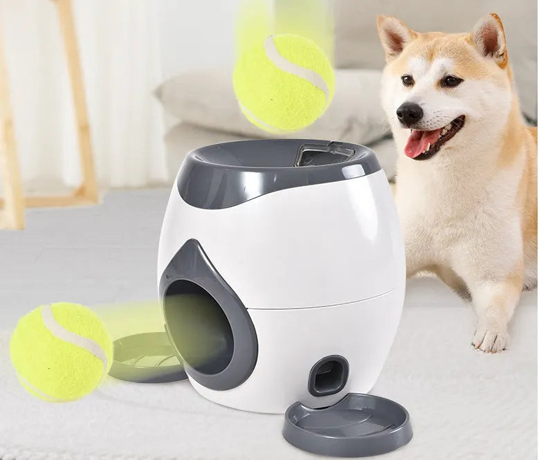 Smart pet feeder reward machine with two tennis balls and treat dispenser in green and white colour, shown on a wooden floor