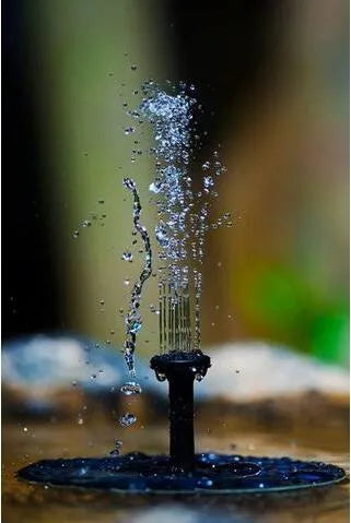 Black solar fountain pump with four spray nozzles on a green grass background next to a birdbath.