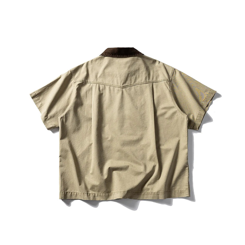 A man wearing a khaki-coloured, loose-fit, short-sleeve cotton overalls shirt for casual leisure.