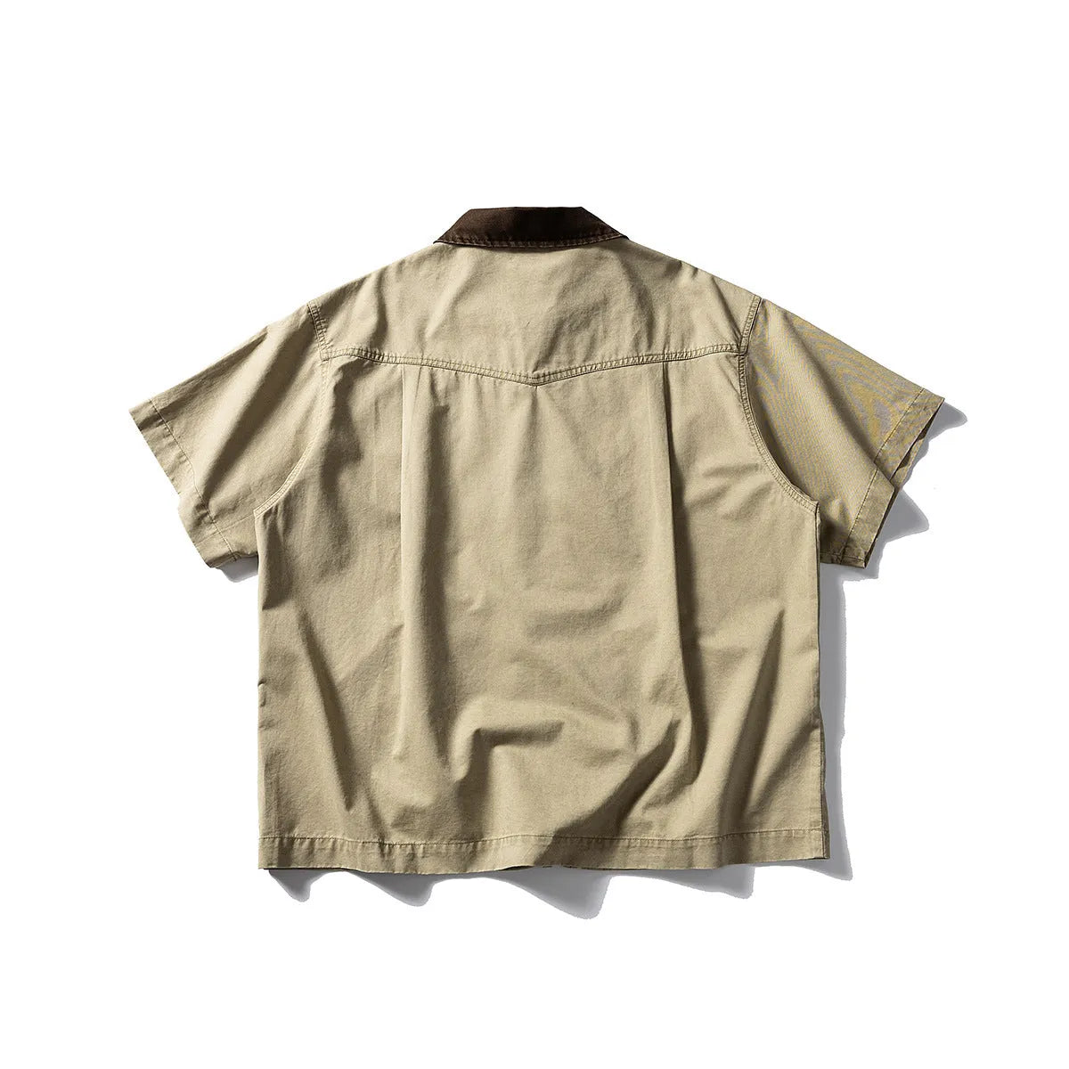 A man wearing a khaki-coloured, loose-fit, short-sleeve cotton overalls shirt for casual leisure.