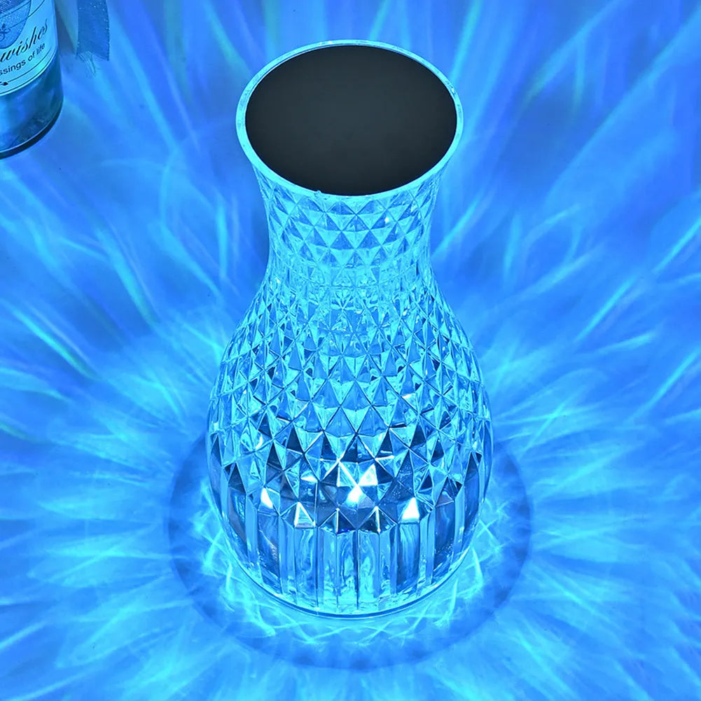 Vase-shaped transparent crystal bedside lamp with touch controls and LED lights on a table.