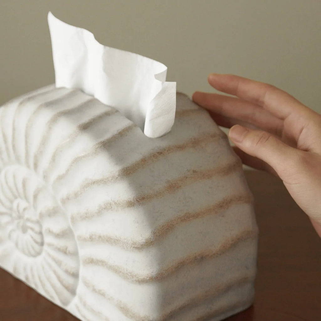 White conch ramble shell design resin tissue box holder on a table.
