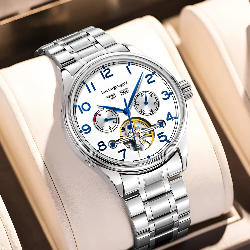 Men's stainless steel mechanical watch with leather strap and butterfly buckle on a business suit cuff.