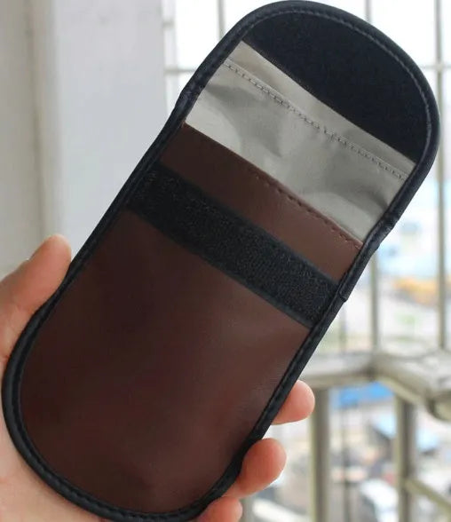Black microfiber Faraday cage pouch for blocking car key and RFID card signals on a table.