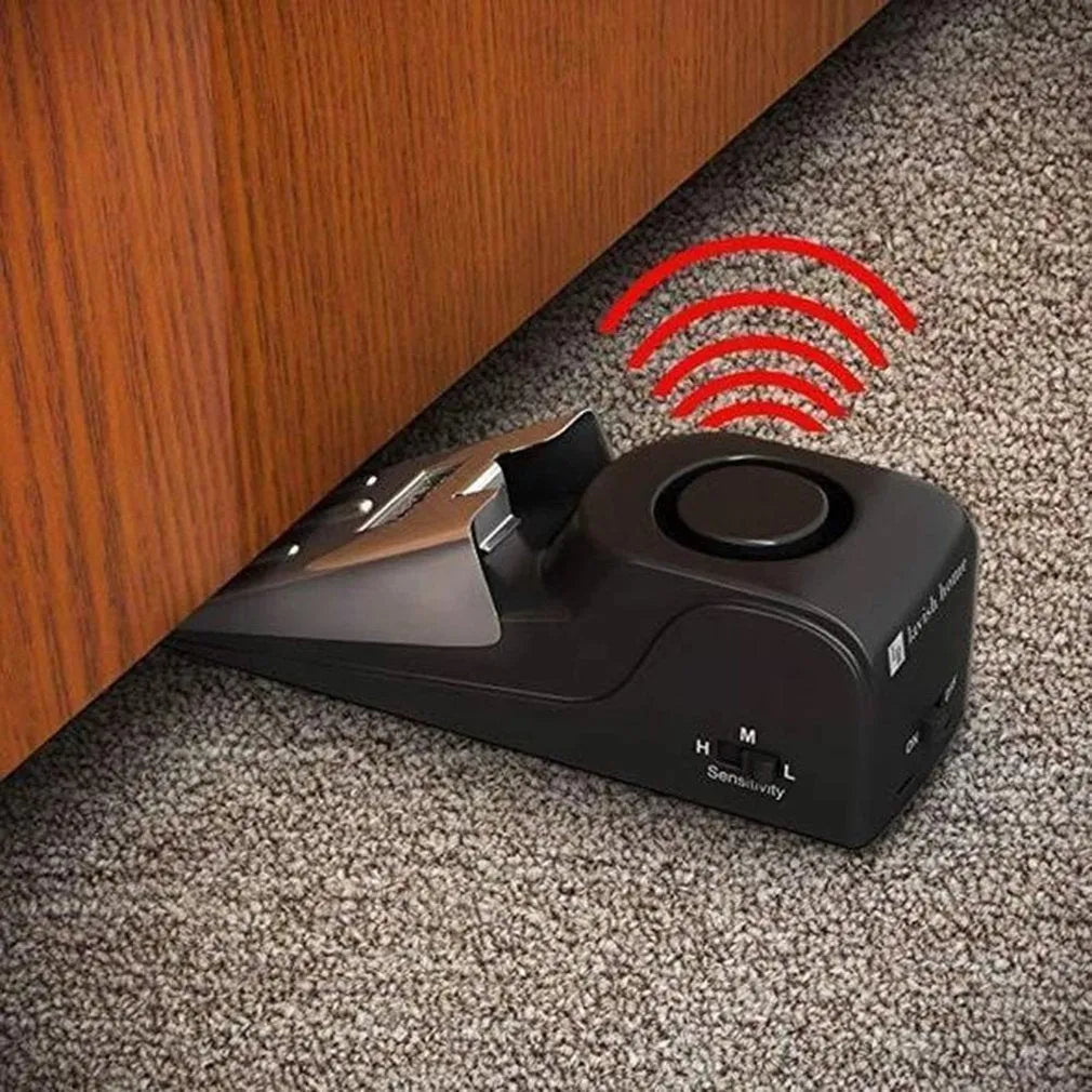 Black portable door stop alarm with wedge shape and stainless steel cover on a wooden floor.